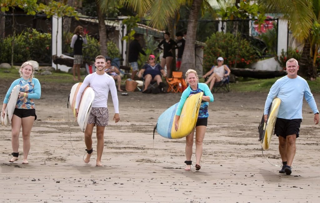 Family walking on Jaco Beach with surfboards, Costa Rica